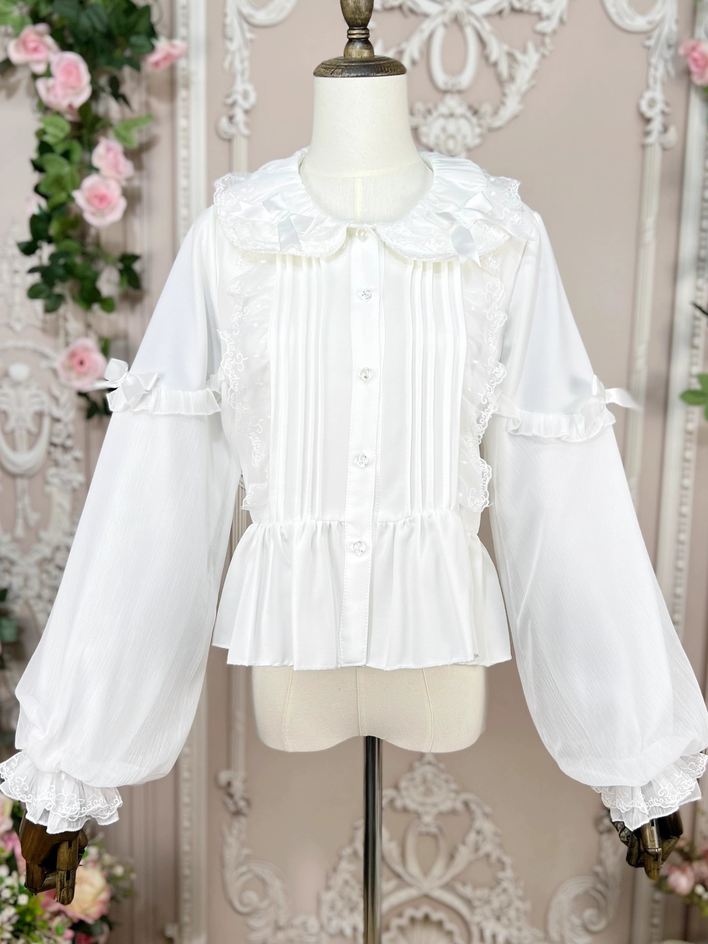 This classic Lolita blouse features a delicate Peter Pan collar and soft bishop sleeves with subtle puff detailing. Rendered in timeless black and white, its accordion pleats and bloom-inspired ruffles add vintage charm to any coordination. The lightweight fabric and tailored fit make it ideal for layering under jumpers or dresses, blending doll-like sweetness with elegant Gothic sophistication for daily wear or special occasions.