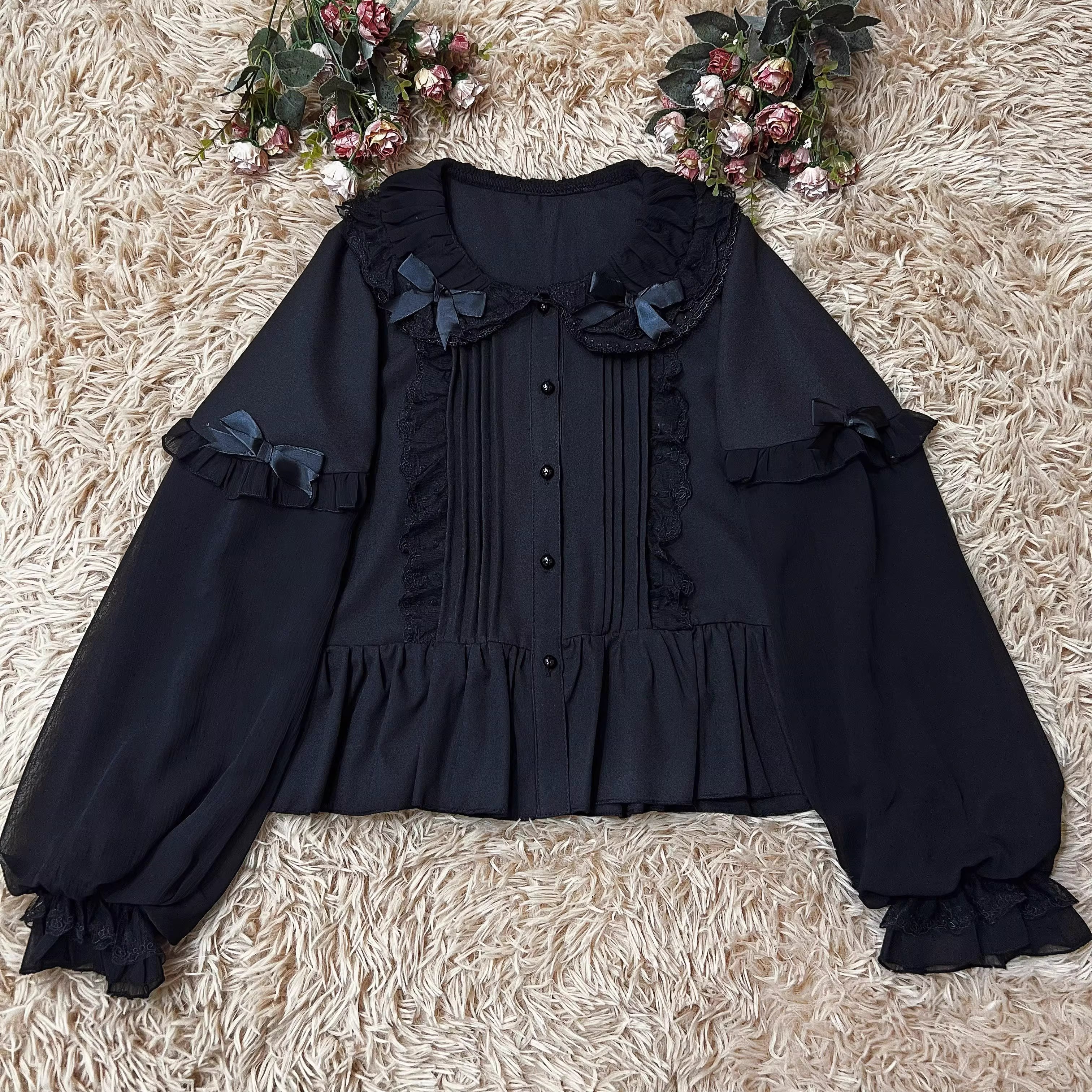 This classic Lolita blouse features a delicate Peter Pan collar and soft bishop sleeves with subtle puff detailing. Rendered in timeless black and white, its accordion pleats and bloom-inspired ruffles add vintage charm to any coordination. The lightweight fabric and tailored fit make it ideal for layering under jumpers or dresses, blending doll-like sweetness with elegant Gothic sophistication for daily wear or special occasions.