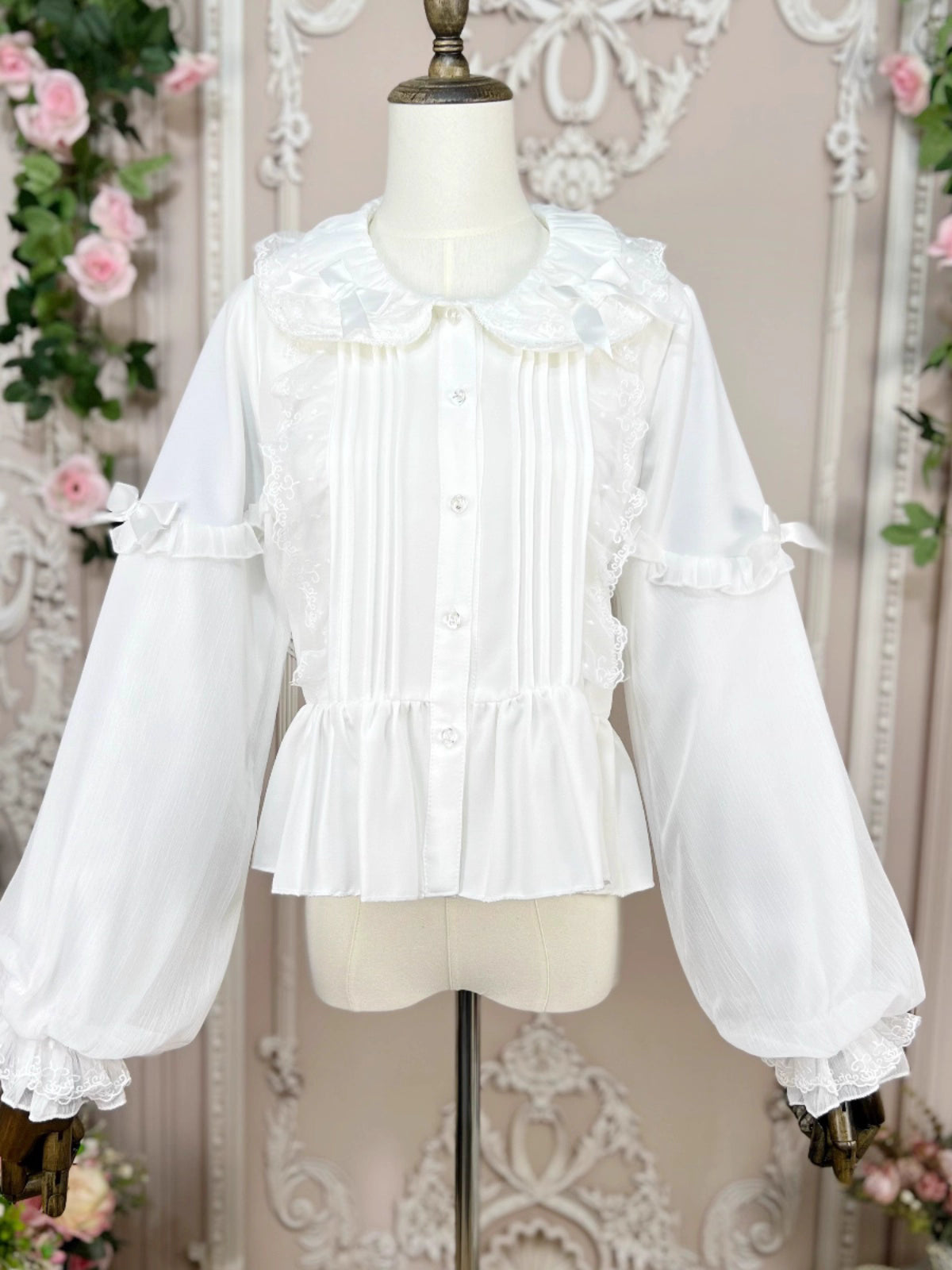 This classic Lolita blouse features a delicate Peter Pan collar and soft bishop sleeves with subtle puff detailing. Rendered in timeless black and white, its accordion pleats and bloom-inspired ruffles add vintage charm to any coordination. The lightweight fabric and tailored fit make it ideal for layering under jumpers or dresses, blending doll-like sweetness with elegant Gothic sophistication for daily wear or special occasions.