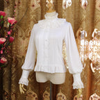 This vintage-inspired blouse features an elegant stand collar and delicate ruffled sleeves crafted from lightweight chiffon. The tailored fit and button-front design create a flattering silhouette, perfect for layering under jumpers or dresses. Its timeless elegance blends retro charm with Lolita sophistication, making it ideal for both classic and sweet coordinates.