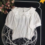 Crafted from breathable cotton, this charming short-sleeve blouse features a classic Peter Pan collar and delicate bow tie. The playful plaid pattern in multiple colors offers versatile styling for both Lolita and JK fashion. Its lightweight comfort and sweet design make it ideal for daily wear, effortlessly pairing with jumpers, skirts, or dresses for a fresh, youthful look.