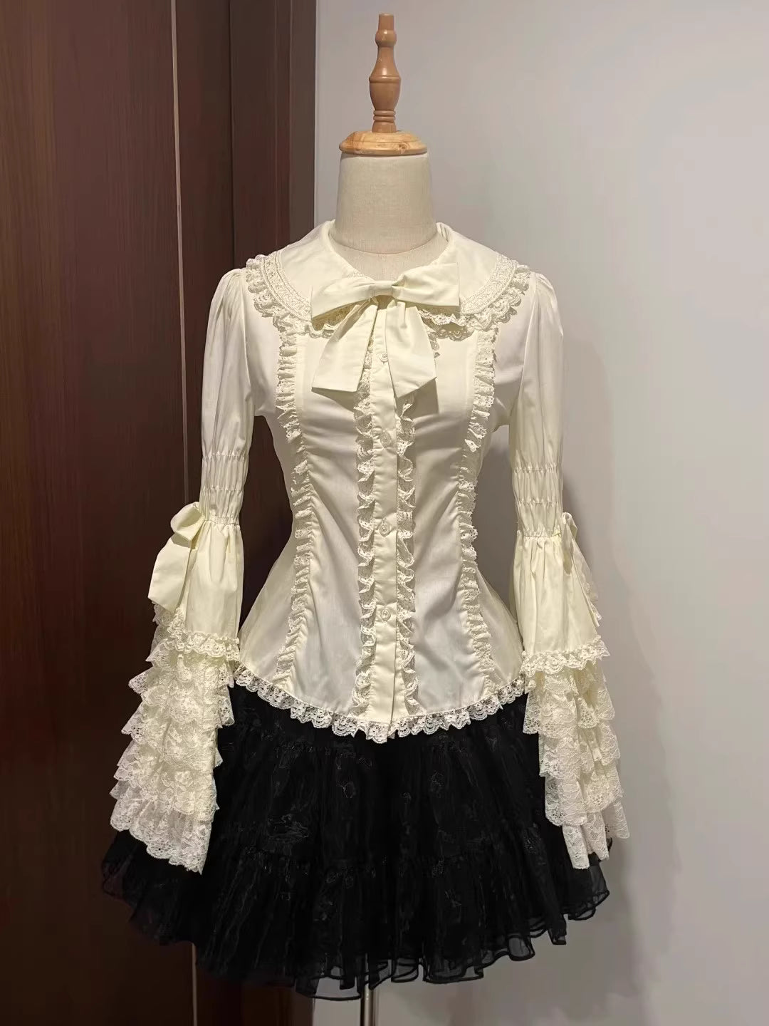 Inspired by antique porcelain dolls and Victorian elegance, this blouse features dramatic gigot sleeves, delicate lace trim, and a tailored yet forgiving fit. The ivory and black color options evoke timeless sophistication, while lightweight fabric ensures comfort. Designed to layer under jumperskirts or wear standalone, it celebrates opulent nostalgia with modern inclusivity. Perfect for creating a poetic, romantic silhouette.