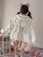 Inspired by fairy-tale whimsy, this hooded cardigan features soft bunny ear details and a playful tie-front design. Crafted from plush, cozy knit, it combines adorable charm with practical warmth for autumn and winter. The creamy white hue and rounded silhouette evoke a sugary sweetness, perfect for layering over dresses or pairing with skirts—a delightful blend of childhood nostalgia and wearable comfort.
